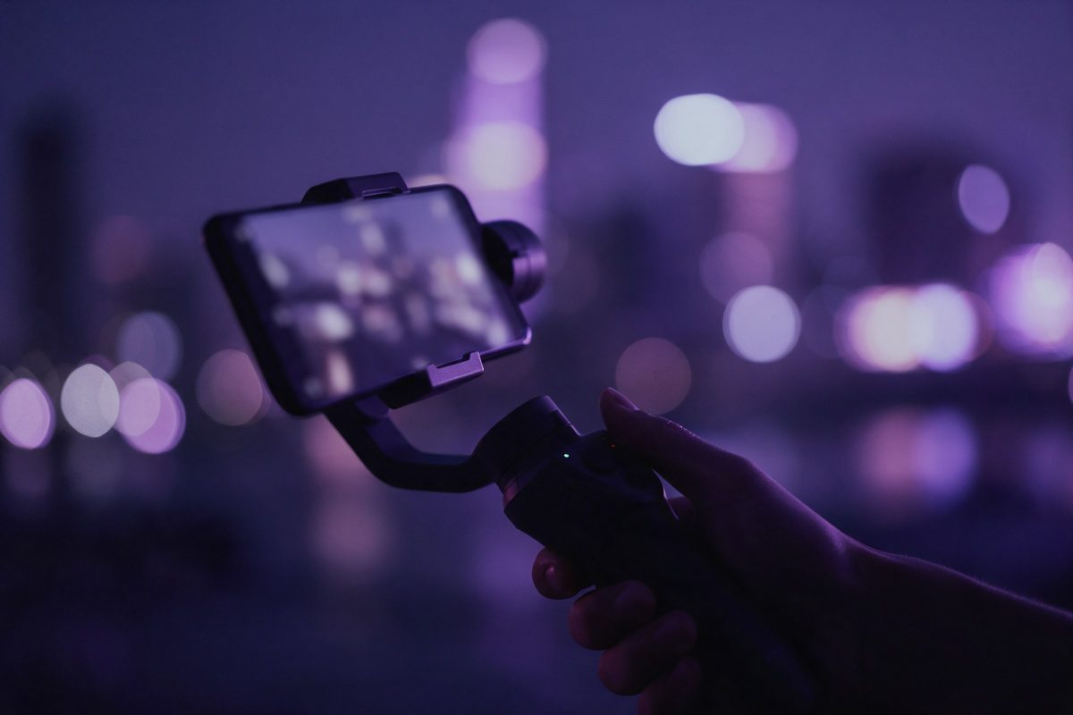 Gece şehir ışıkları önünde gimbal üzerindeki telefonu tutan el